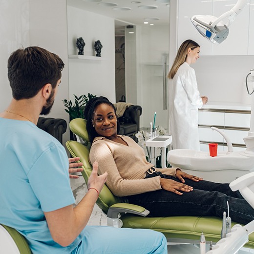 Smiling patient sitting in treatment chair and talking to dentist