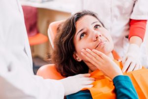 a person holding their mouth while sitting in a treatment chair and speaking with their dentist about why they need a tooth extraction
