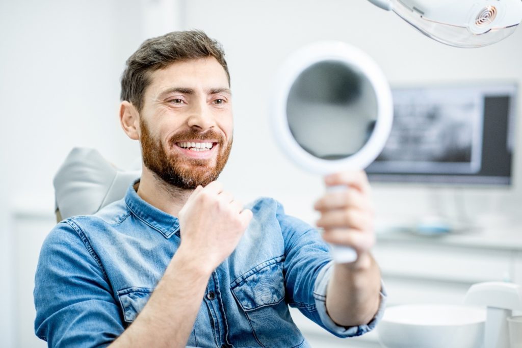 Man with dental implants smiling while looking in mirror